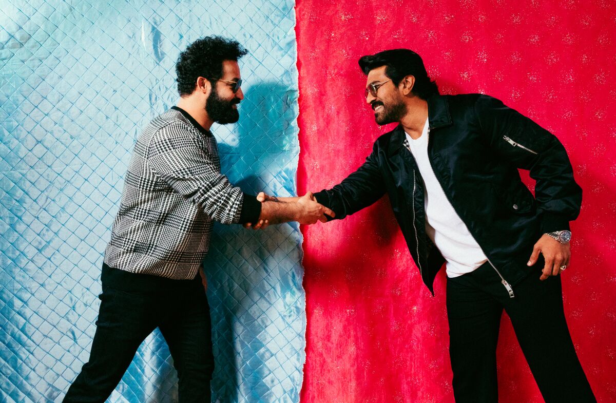 Two men shake hands against a blue and red background.
