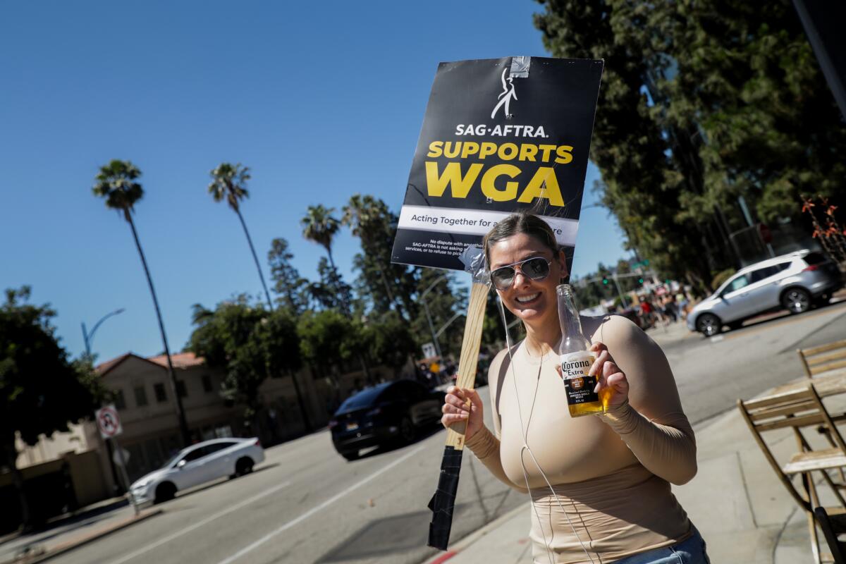 A woman holds a picket sign and a beer