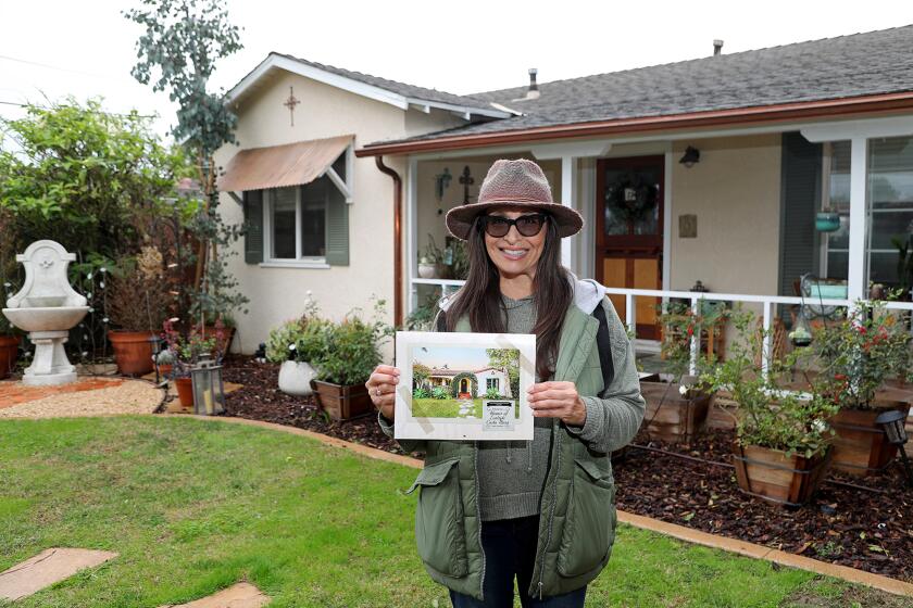 Realtor Renee Pina holds up her 2022 calendar of historic homes in Costa Mesa's east side (1900-1930) as she stands in front of her own 1952 historically renovated home on Thursday in Costa Mesa. Pina became a business-level member of the city's Historical Society in November and came up with an idea to raise awareness and funds for the nonprofit organization.