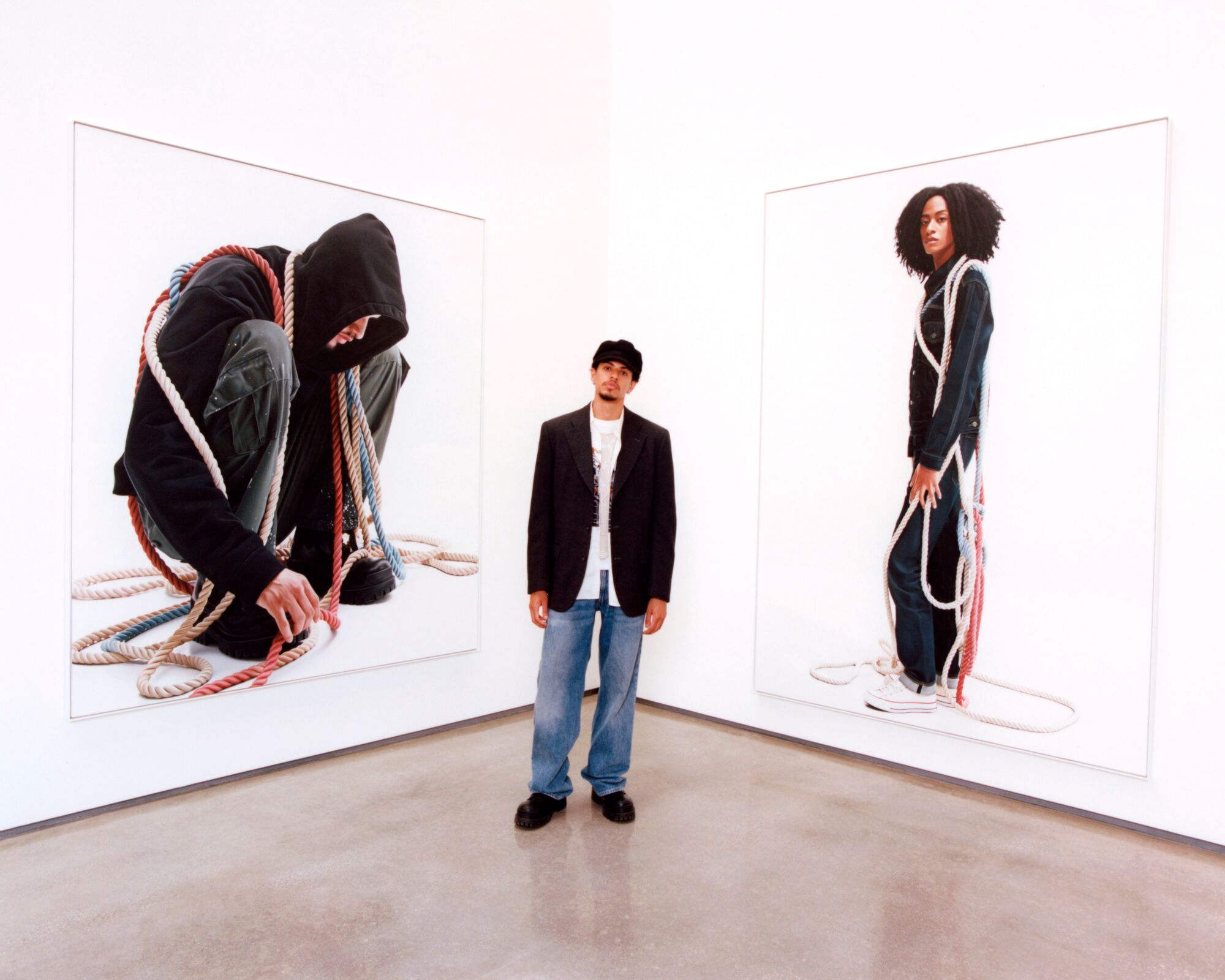 The artist stands between two of his large portraits of people draped in rope.