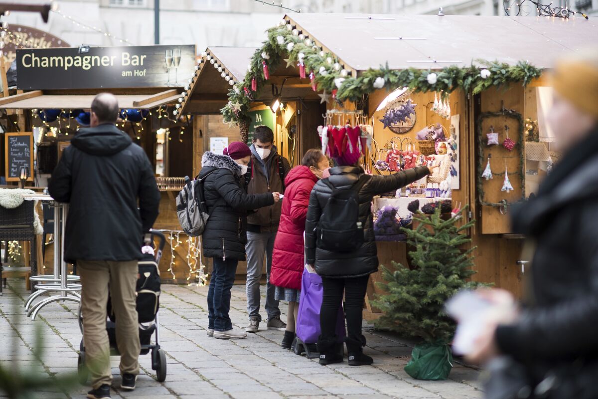 People in masks shop at an outdoor Christmas market.