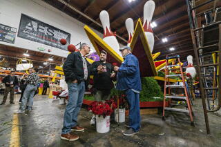 Three men standing near buckets of red roses and a float featuring bowling pins in a warehouse space