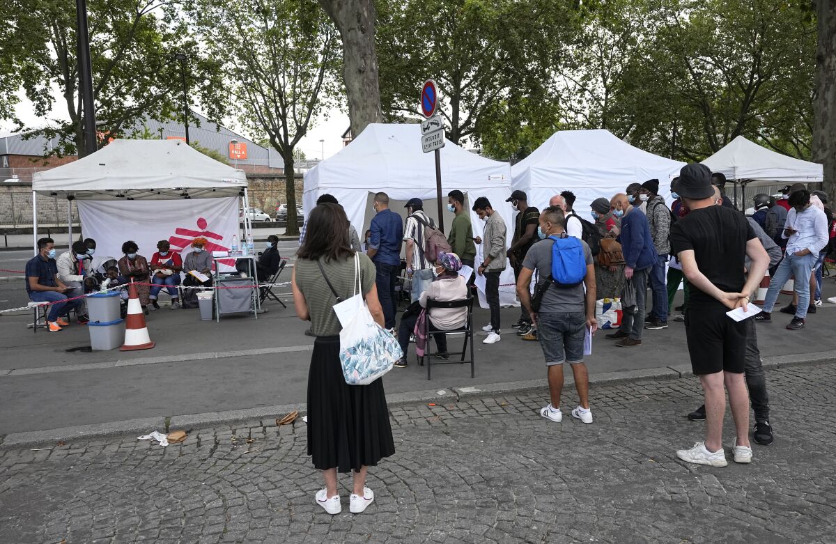 Near a row of white tents, people stand in lines.