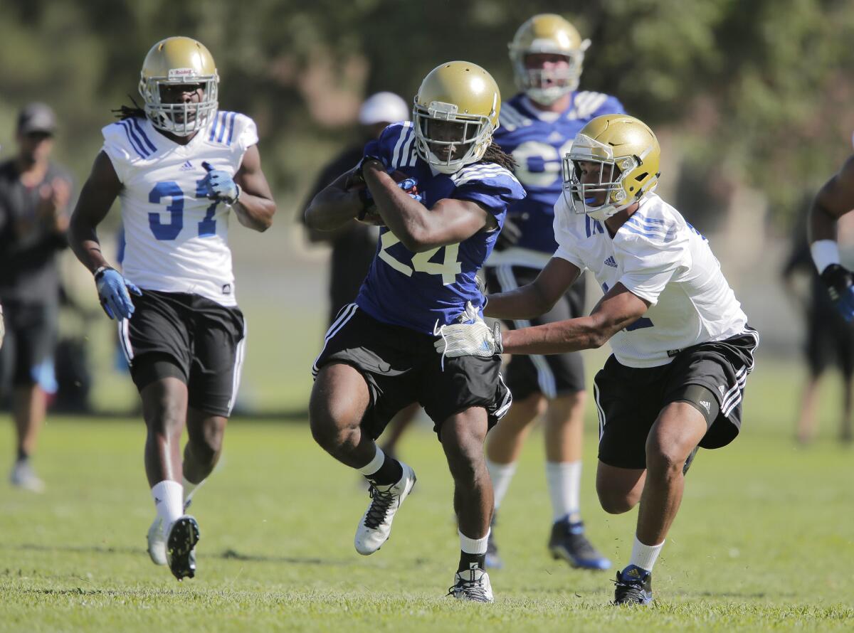 UCLA running back Paul Perkins (24) gains yardage before being touched by defender DeChaun Holiday (17) during the first day of training camp Monday at Cal State San Bernardino.