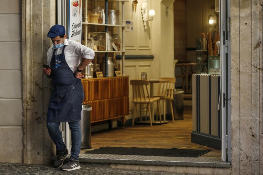 A waiter stands outside a cafe in downtown Rome, Sunday, Oct. 25, 2020. For at least the next month, people outdoors except for small children must now wear masks in all of Italy, gyms, cinemas and movie theaters will be closed, ski slopes are off-limits to all but competitive skiers and cafes and restaurants must shut down in early evenings, under a decree signed on Sunday by Italian Premier Giuseppe Conte, who ruled against another severe lockdown despite a current surge in COVID-19 infections. (Cecilia FabianoLaPresse via AP)