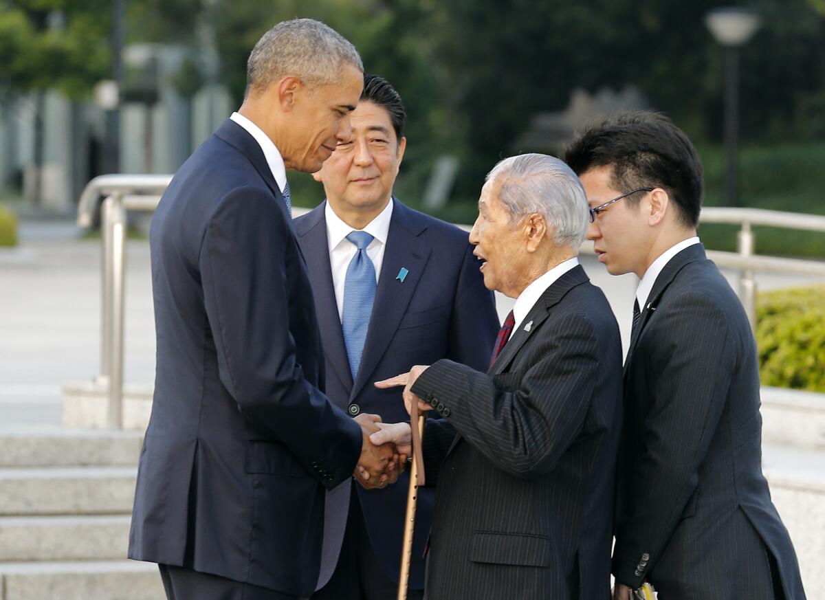 Four men in dark suits, two shaking hands.