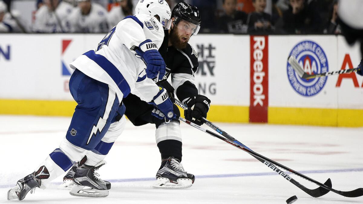 Kings defenseman Jake Muzzin, right, sends the puck up ice while under pressure from Lightning center Tyler Johnson during the second period Monday.