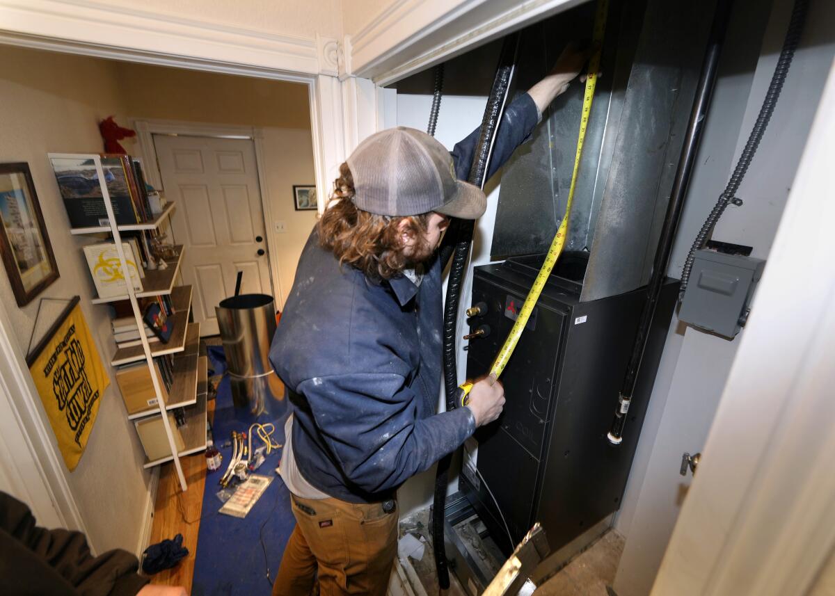John Paul uses a tape measure during the installation of a heat pump in a rowhouse in northwest Denver.