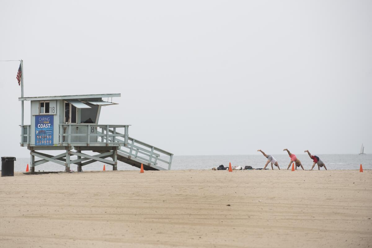 A lifeguard tower on a beach next to three people doing yoga