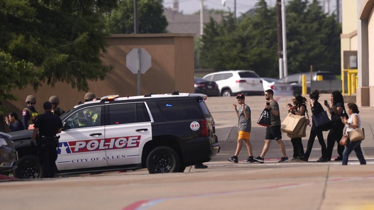 People raise their hands as they leave a shopping center after a shooting in Allen, Texas.