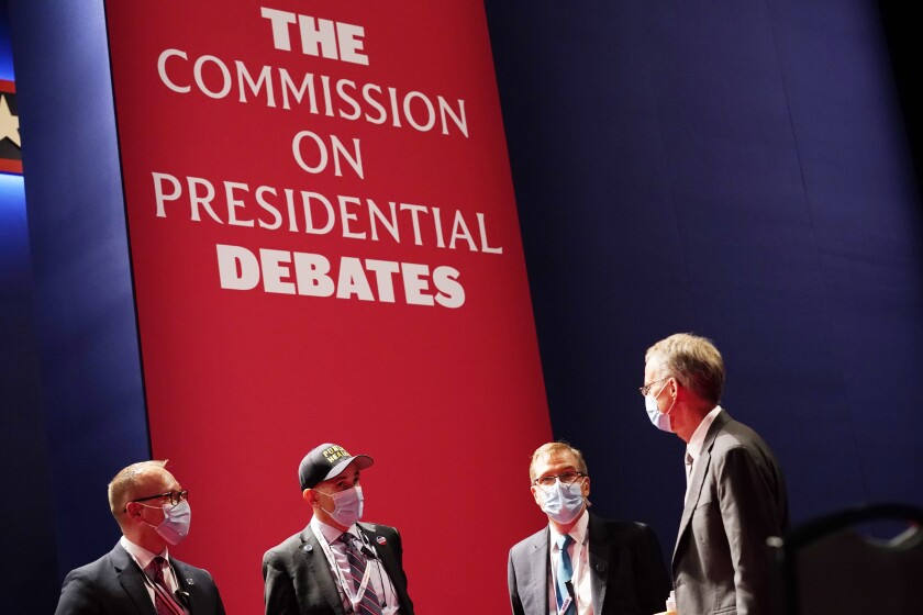Men wearing masks stand near a sign that says "Commission on Presidential Debates"