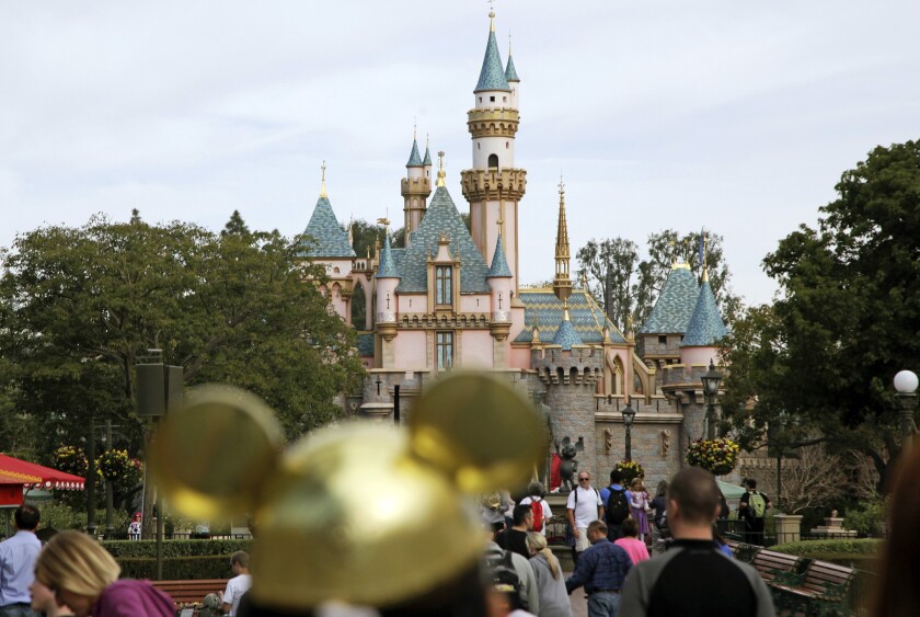People walk toward a castle in the distance. In the foreground is someone with a mouse ears hat.