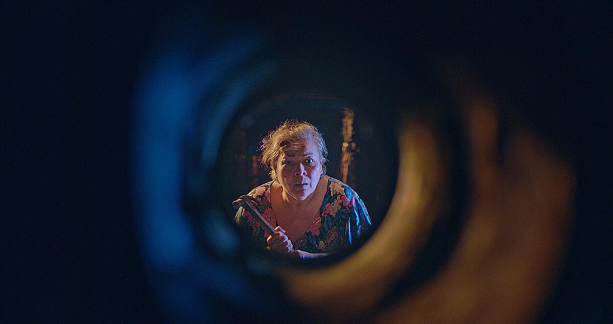 A woman holding a hammer looks through a tunnel.