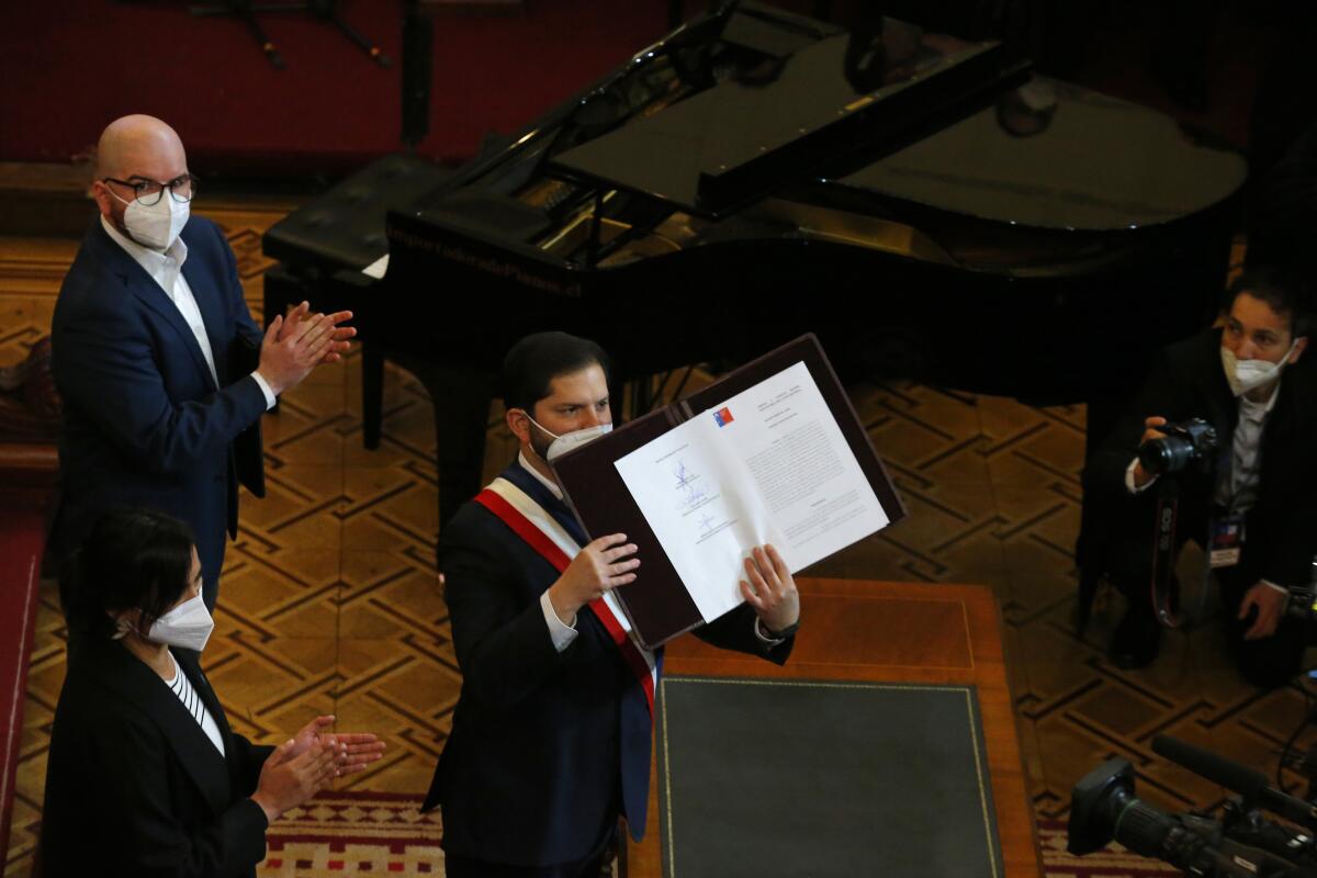 Chilean President Gabriel Boric holds up the final version of the country's proposed, new constitution during a ceremony at the former Congress in Santiago, Chile, Monday, July 4, 2022. Chileans elected an assembly to write fresh governing principles and put them to a national vote in 2022 with the goal of a more inclusive country and the erasure of a relic of military rule. (AP Photo/Luis Hidalgo)