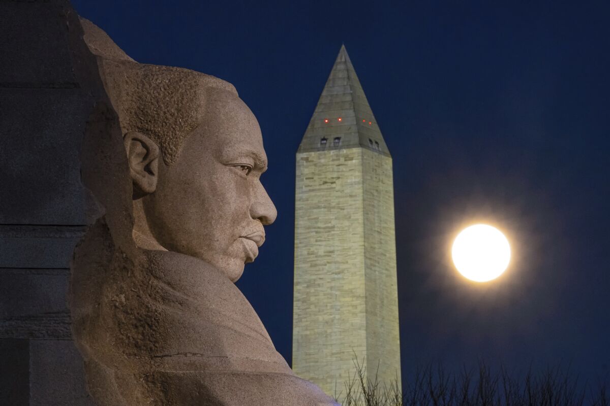 The rising full moon passes behind the Martin Luther King Memorial and the Washington Monument.