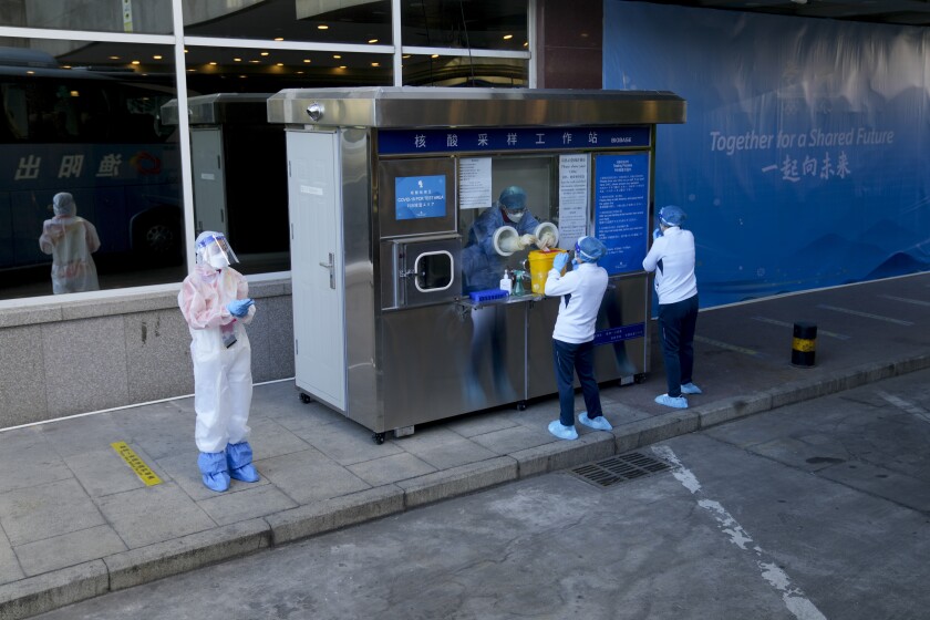 Workers wearing protective gear stand outside a venue at the Beijing Winter Olympic Games.