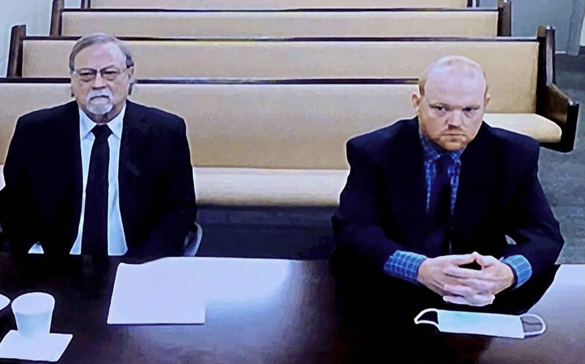 In this image made from video, from left, father and son, Gregory and Travis McMichael, accused in the shooting death of Ahmaud Arbery in Georgia on Feb. 2020, listen via closed circuit tv in the Glynn County Detention center in Brunswick, Ga., on Thursday, Nov. 12, as lawyers argue for bond to be set at the Glynn County courthouse. The McMichaels chased and fatally shot Ahmaud Arbery, a 25-year-old Black man, after they spotted him running in their neighborhood just outside the port city of Brunswick.(AP Photo/Lewis Levine)