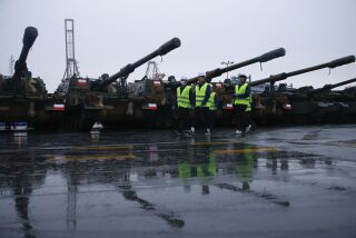La delegación surcoreana camina junto a los cañones Thunder K9 en el puerto de la armada polaca en Gdynia, Polonia, martes 6 de diciembre de 2022. El presidente polaco Andrzej Duda y su ministro de Defensa recibieron el primer envío de tanques y cañones de Corea del Sur.(AP Foto/Michal Dyjuk)