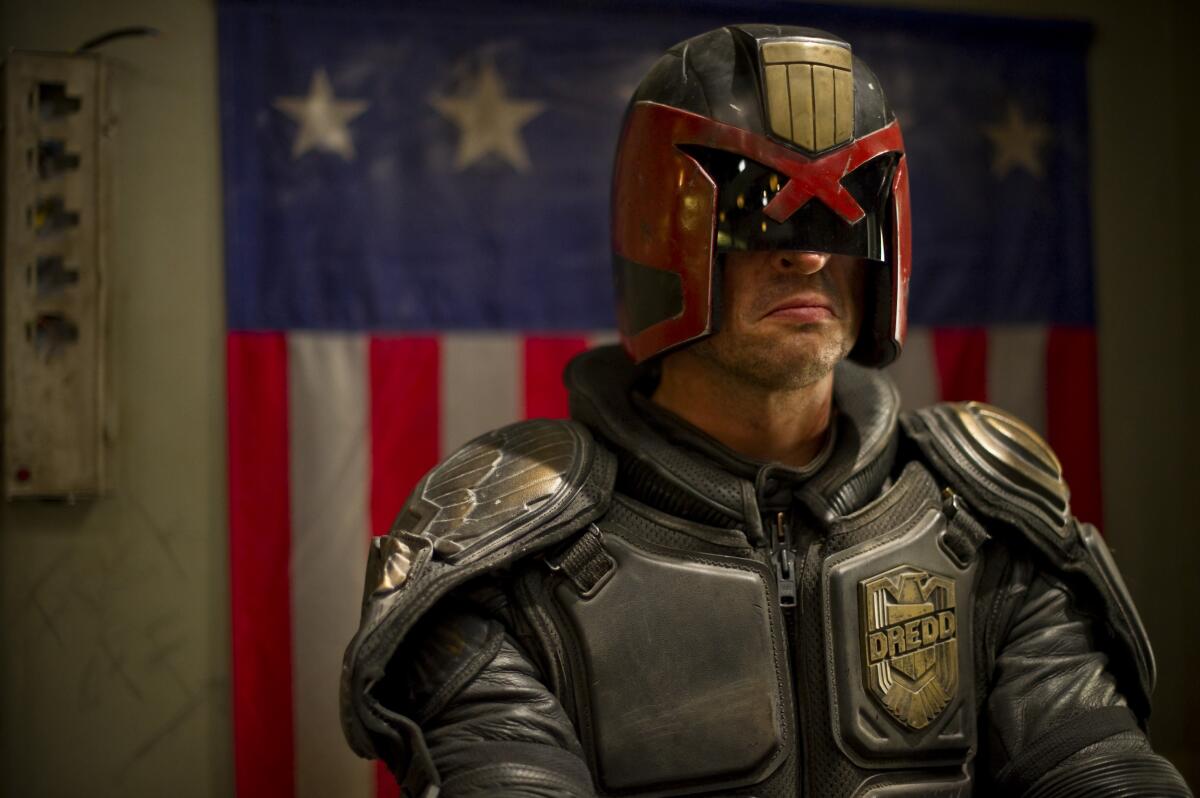 A futuristic law enforcement officer wears a helmet, body armor and a permanent scowl
