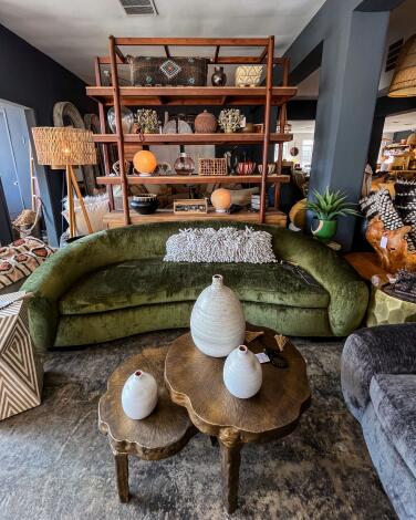 A green velvet semicircular sofa sits in front of a tchotchke-covered shelf at the Joneses. 