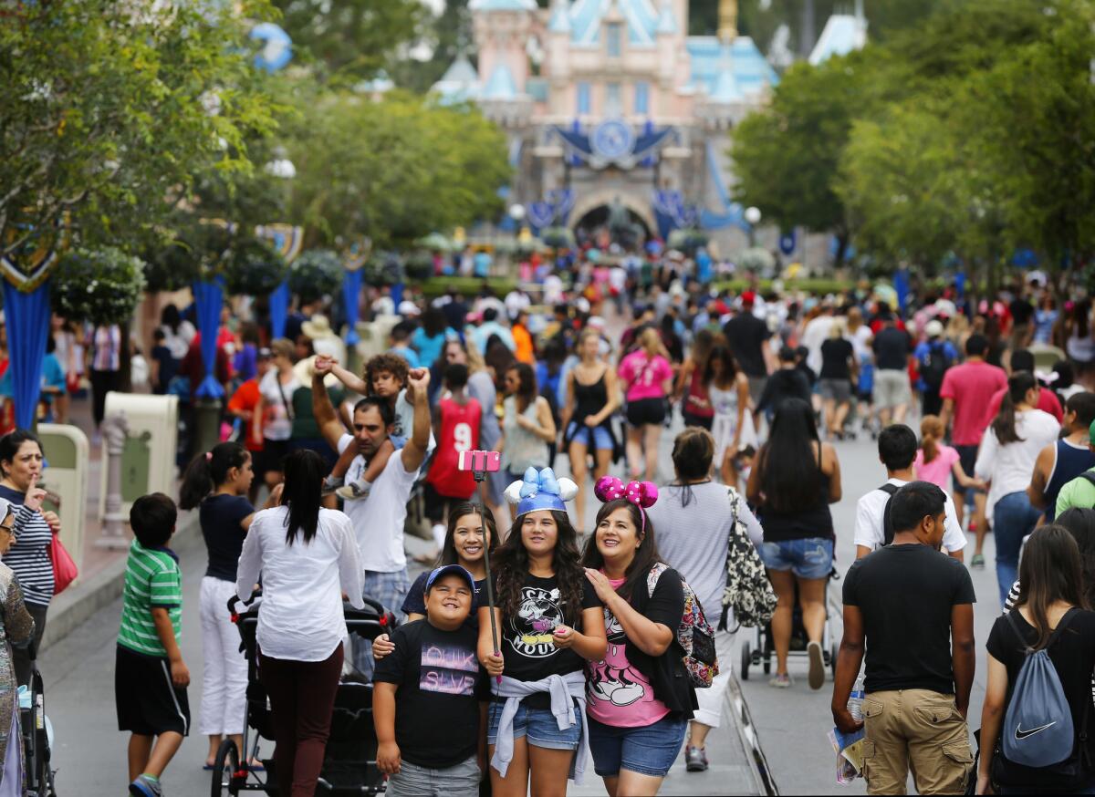 Visitors pause for a selfie in front of a crowded Disneyland's Sleeping Beauty Castle. 