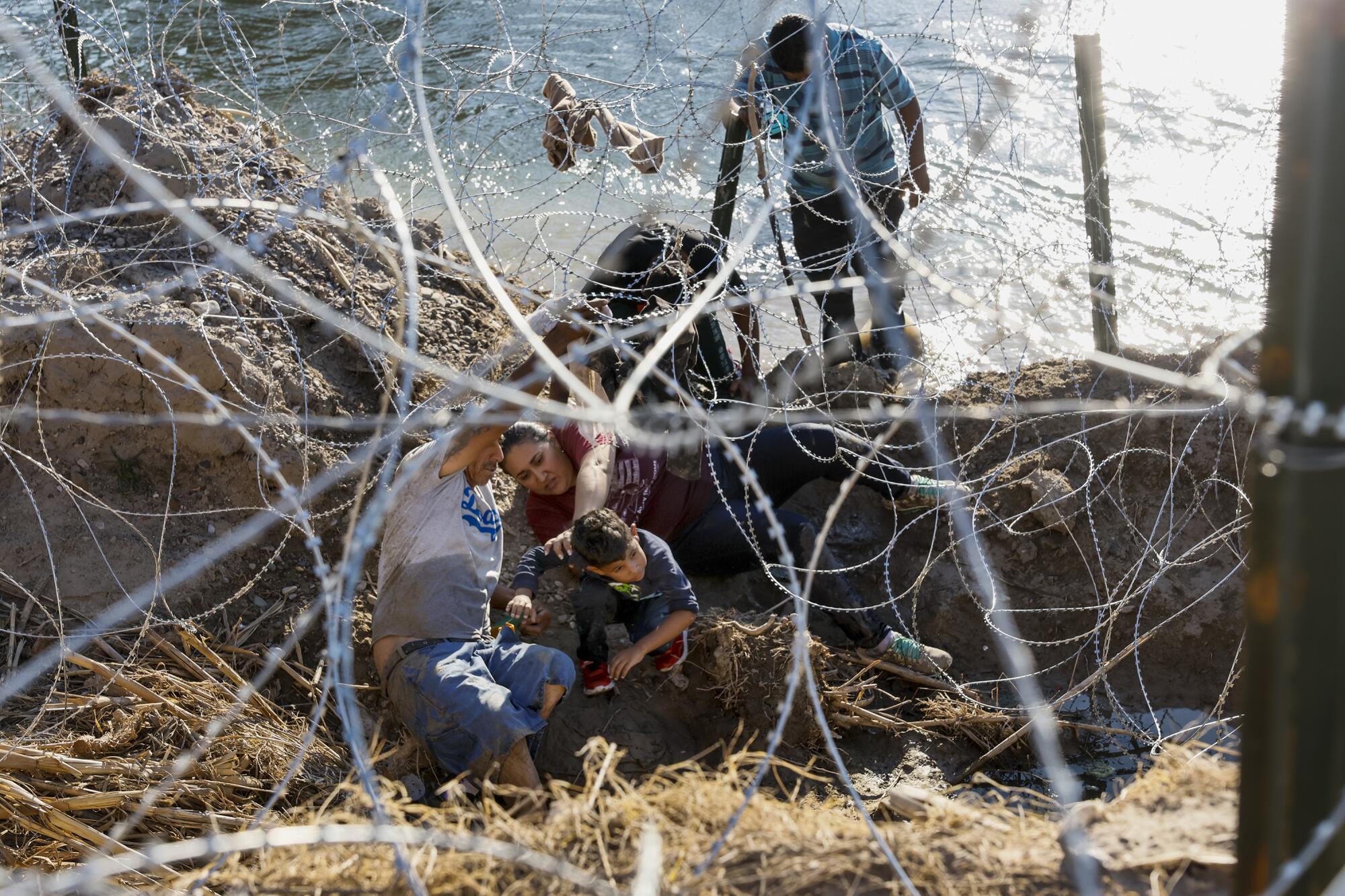 A man lifts up a snarl of razor wire so his young son and wife can crawl under as others follow