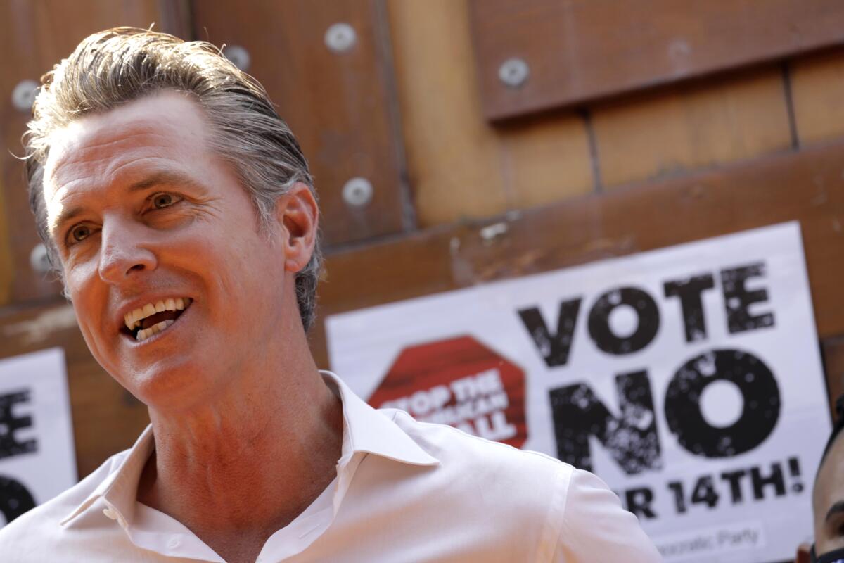 California Gov. Gavin Newsom stands in front of an anti-recall sign