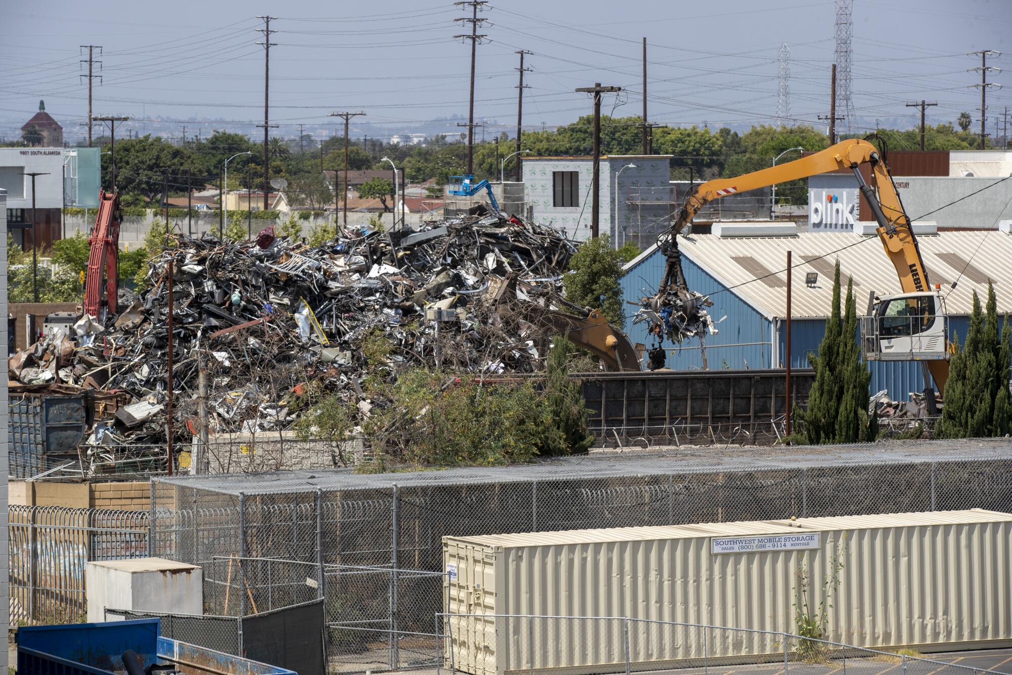 A crane arm lifts metal from a giant scrap heap.
