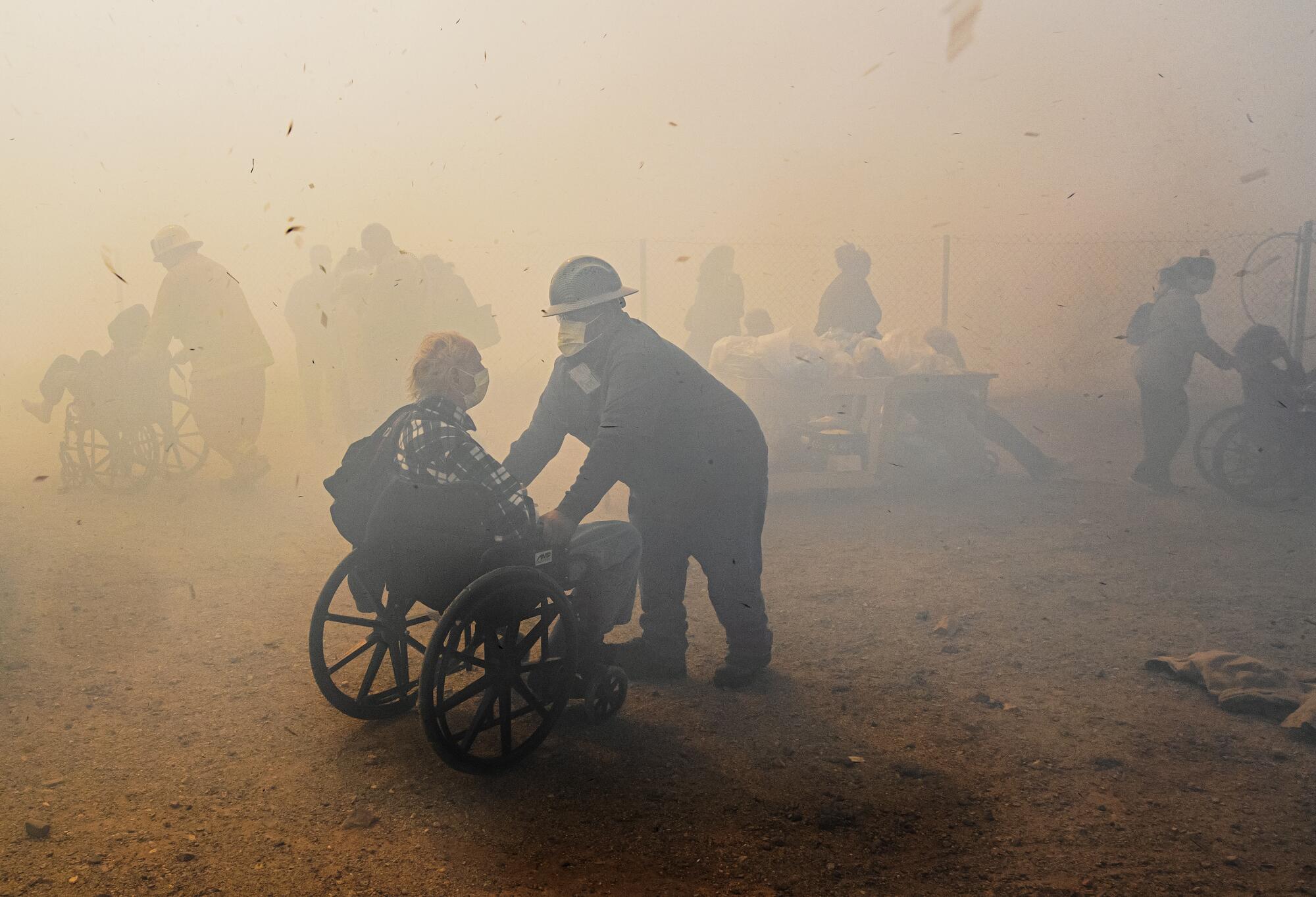 Workers help people in wheelchairs outside in smoky air.