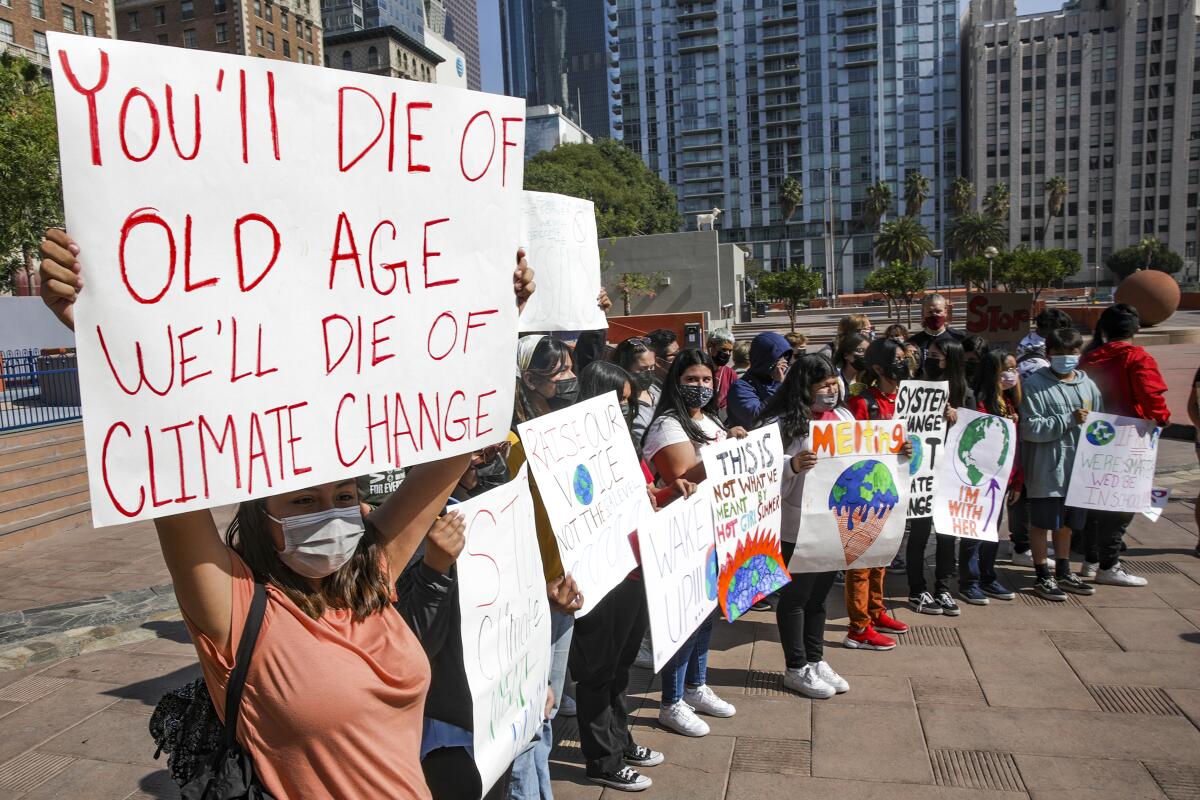 Young people, masked to protect against COVID,  hold up signs  urging action on climate change.