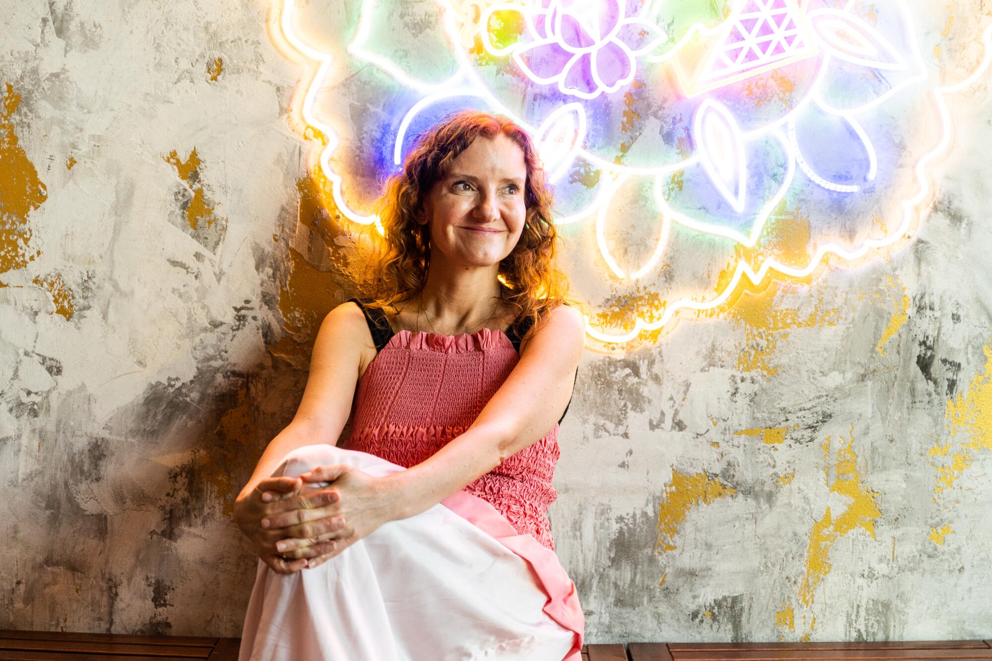 Elena Reygadas, seated and leaning back on a floral and neon wall behind her 