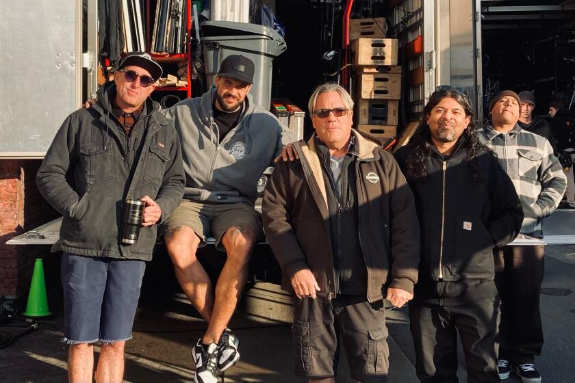 Five men in jackets posing in front of a truck full of production equipment.