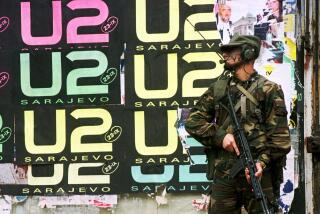 A soldier stands in front of a U2 poster.