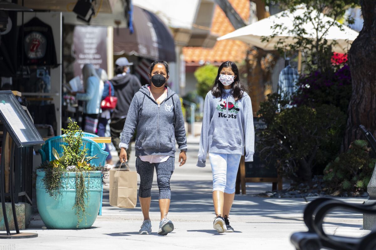 Two masked women stroll on a sidewalk