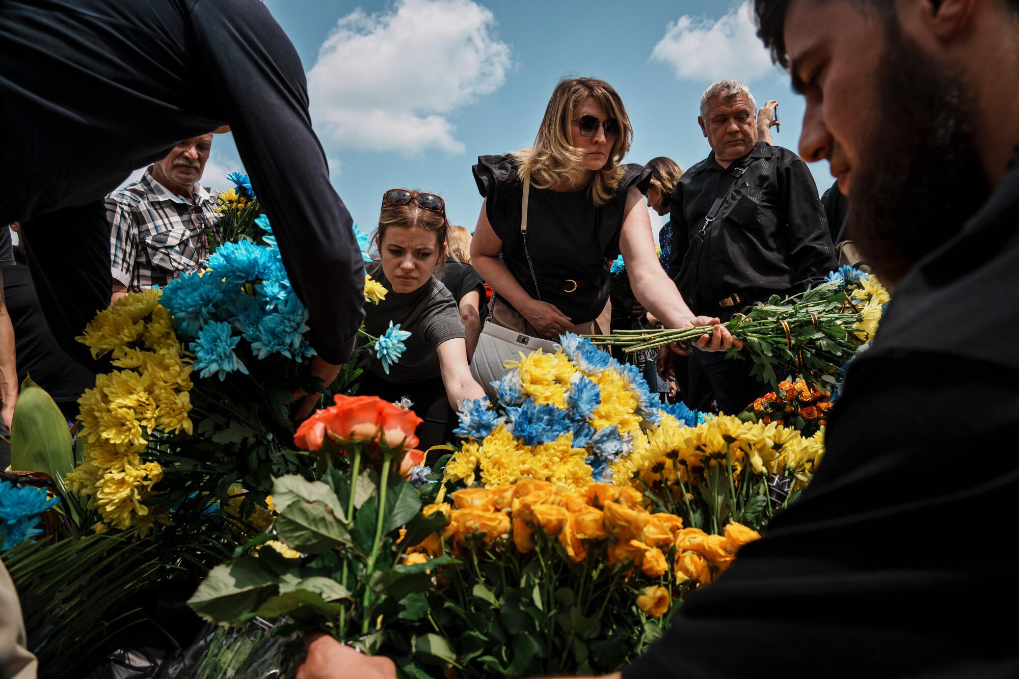 Mourners put mostly yellow and blue flowers on a gravesite 