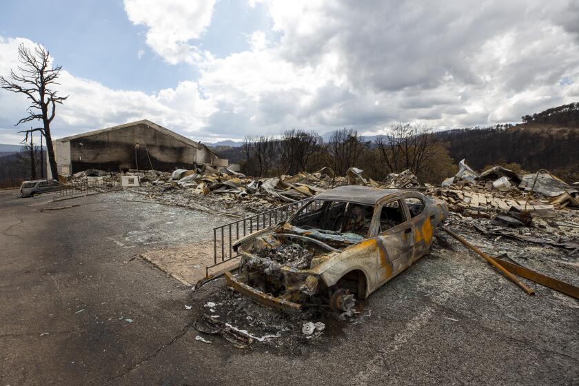 A charred car and the remains of the Swiss Chalet Hotel are shown after it was destroyed by the South Fork Fire in the mountain village of Ruidoso, N.M., Saturday, June 22, 2024. (AP Photo/Andres Leighton)