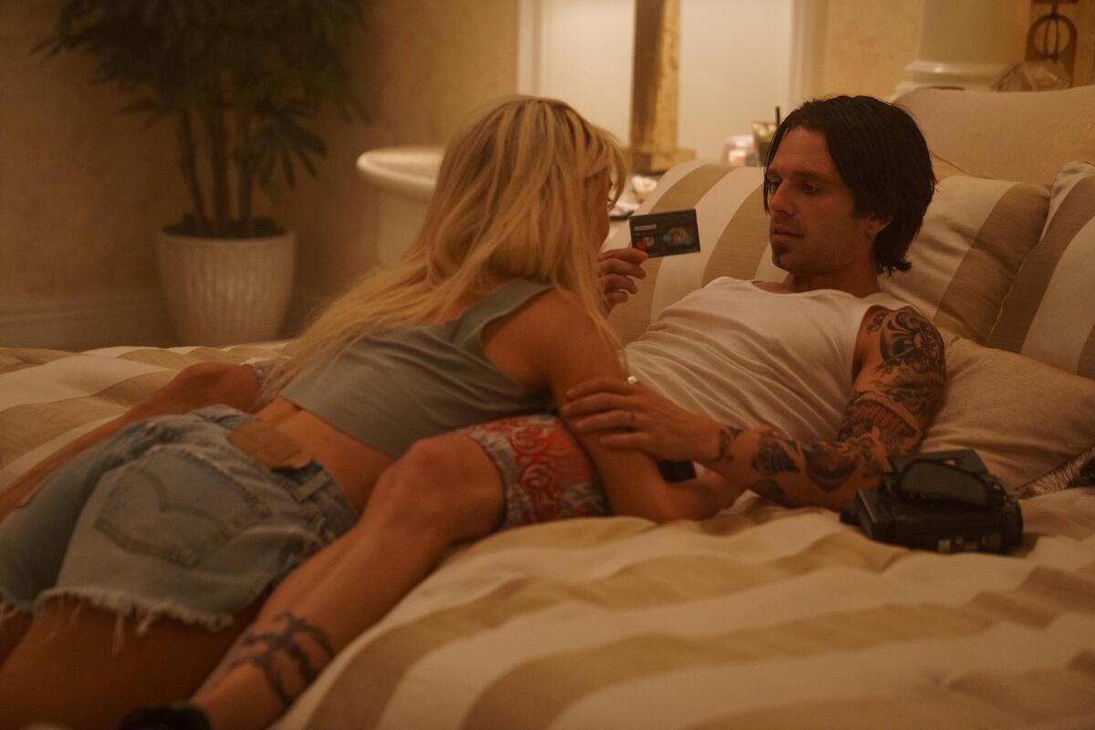 A woman and a man lie in bed with a video camera