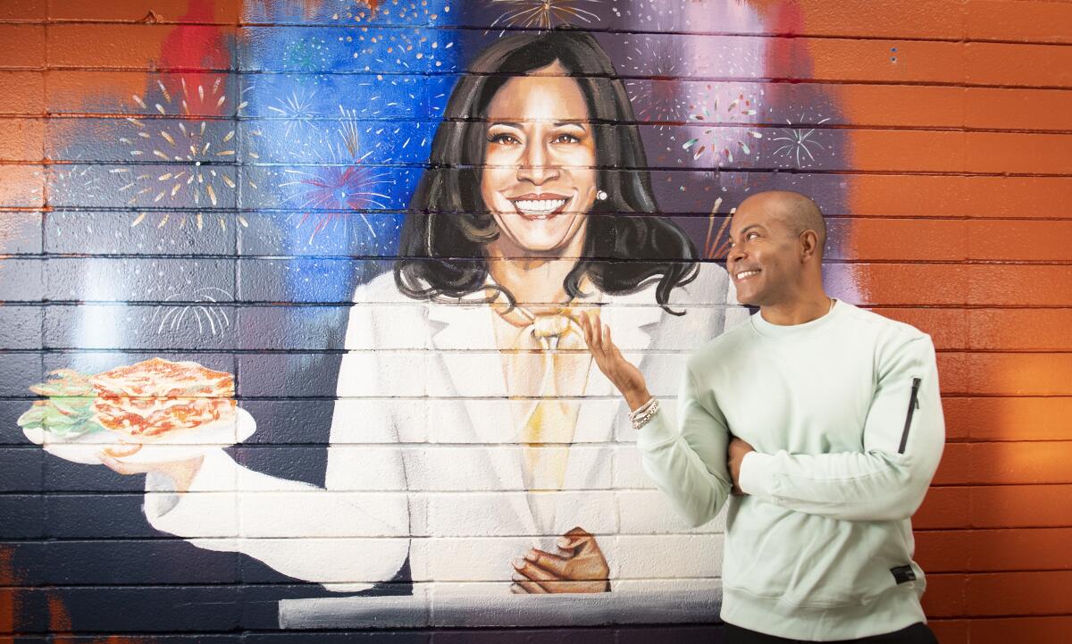Derreck Johnson, founder of the Home of Chicken and Waffles, stands in front of a Kamala Harris mural.