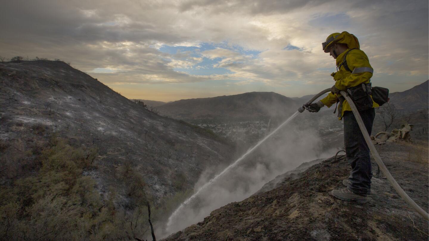 LA County firefighter Kevin Sleight extinguishes hot spots while battling the La Tuna Canyon fire along Crestline Drive Sunday.