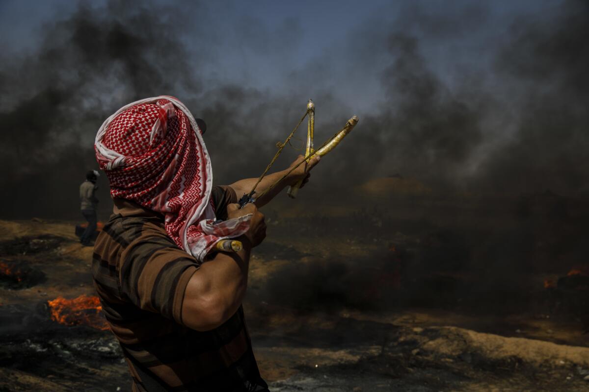 Under the shroud of smoke from the burning tires, a Palestinian man aims a projectile towards the border fence separating Israel and the Gaza Strip during the Great March of Return protest in a camp east of Khan Younis, Gaza Strip.