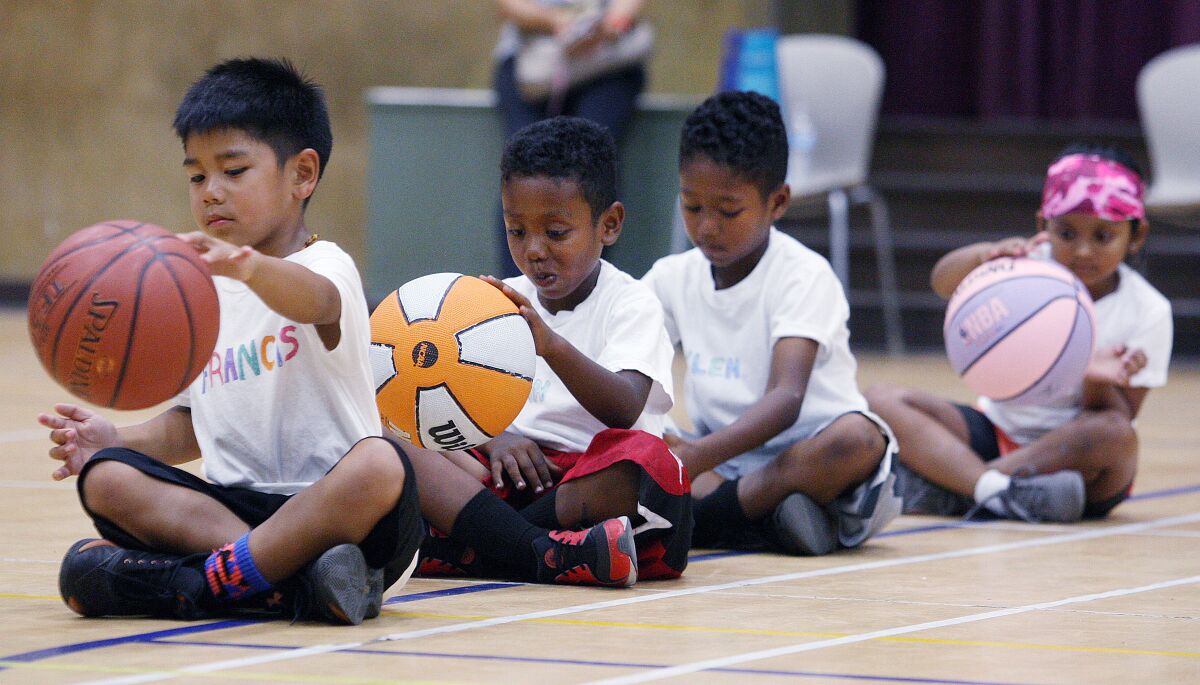 A line of four children sitting cross-legged and dribbling basketballs