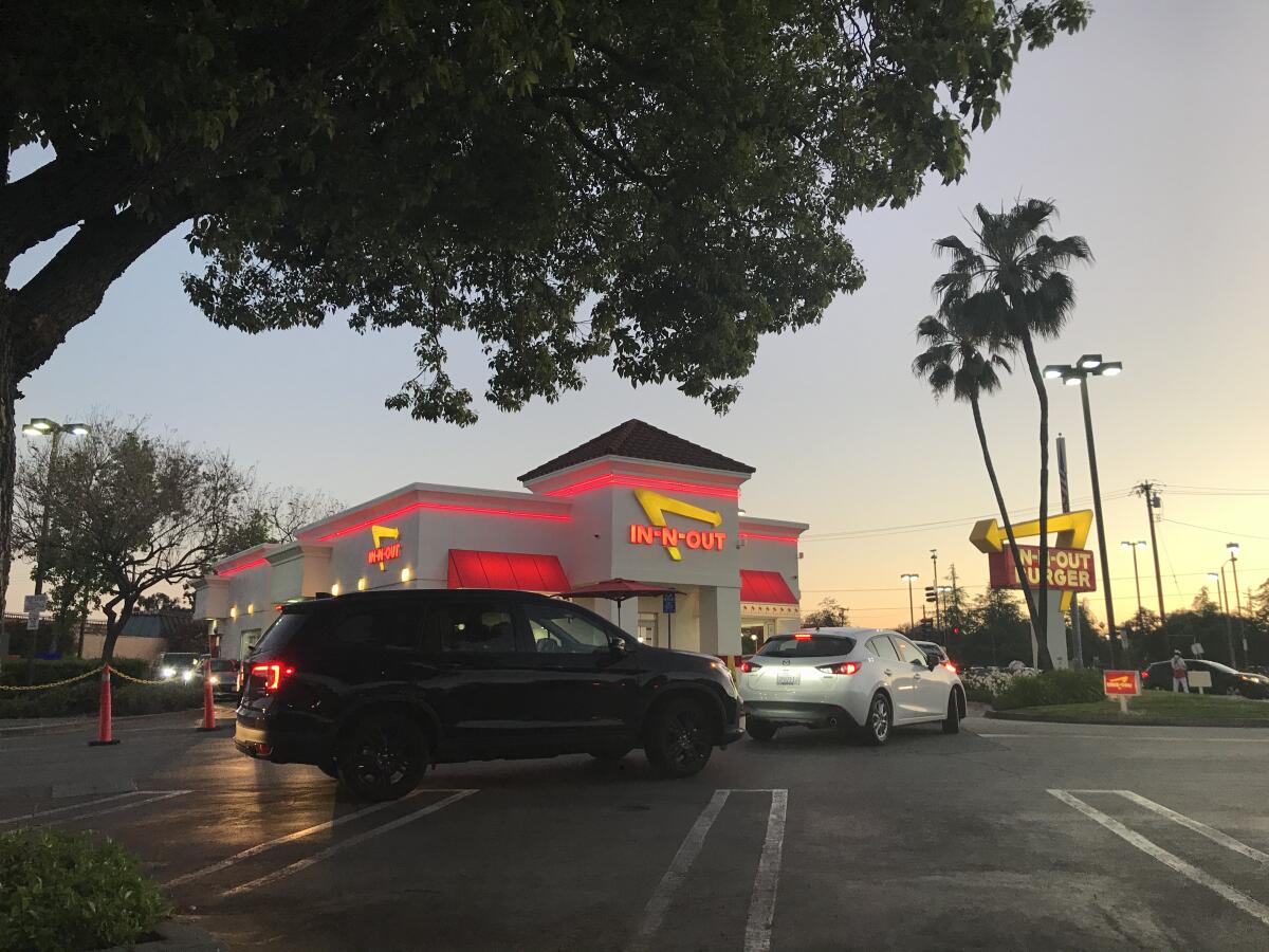 Taillights on cars light up in a parking lot outside an In-N-Out at dusk.