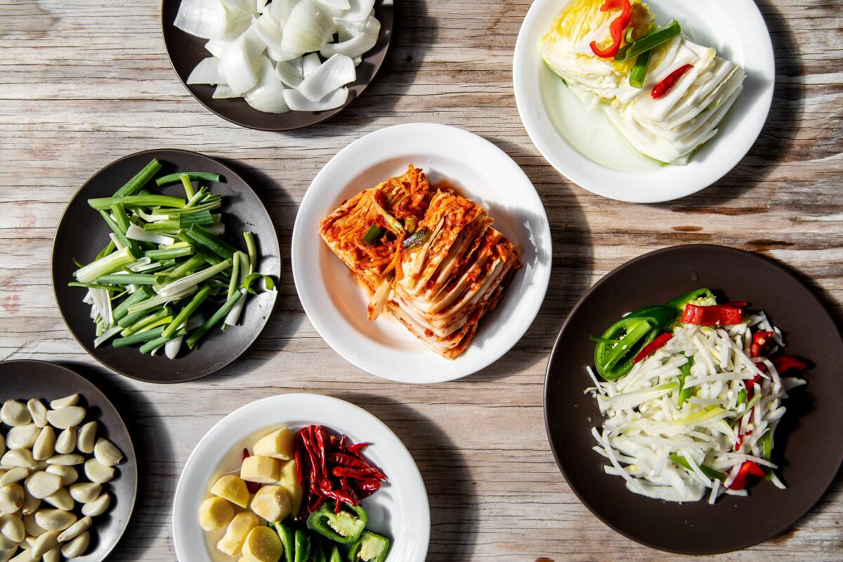 A plate of both white and spicy kimchi surrounded by an array of raw ingredients