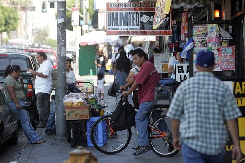 Pedestrians, street vendors and bicyclists crowd a city sidewalk along a row of storefronts