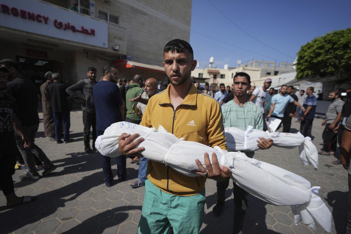 Men each carry the body of a child wrapped in white sheets through the street. 