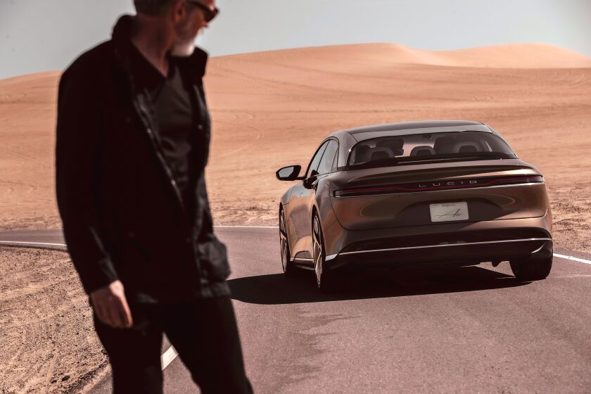 An unidentified man in a flat desert scene looks at a Lucid Air electric car in a 2020 promotional photograph. 