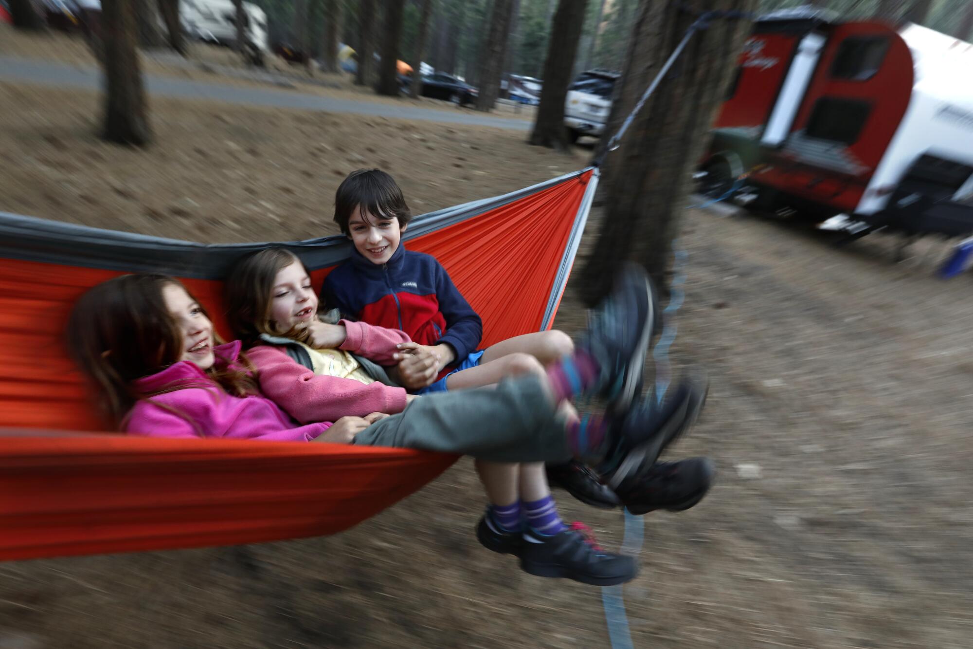 Three young children swing in a red hammock