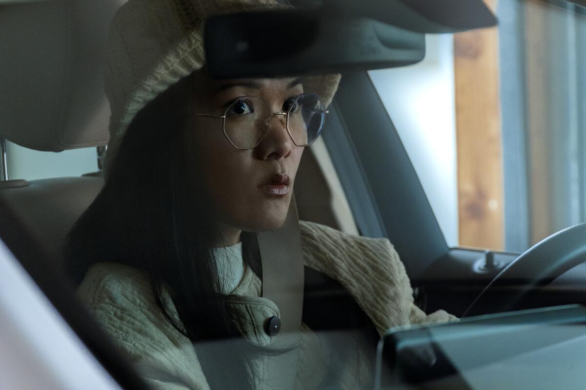 A woman in glasses behind the wheel of her car.