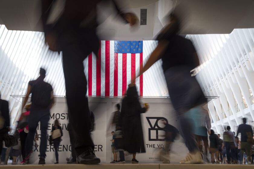 Varias personas caminan frente a la bandera de Estados Unidos dentro de Oculus, parte del centro de transporte del World Trade Center, el 11 de septiembre de 2019, en Nueva York. (AP Foto/Wong Maye-E, archivo)