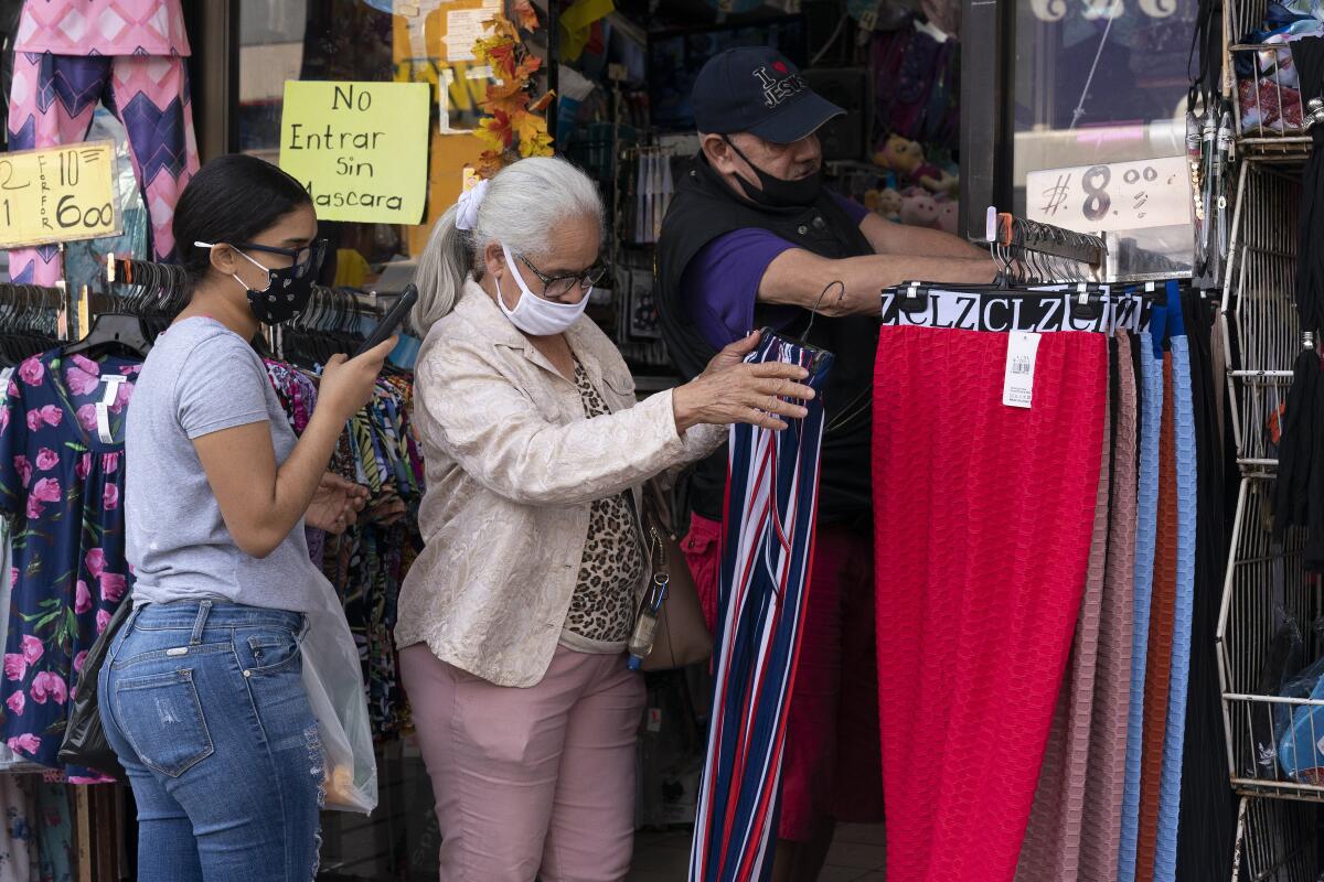 Two masked women browse through clothing racks